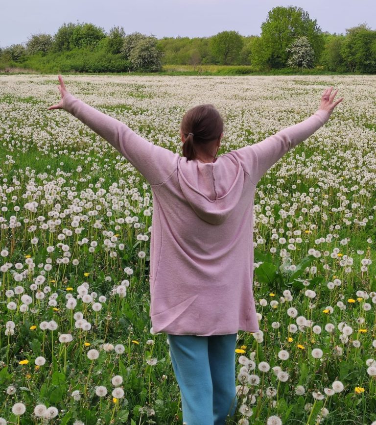 Pusteblumen Eine Frau steht mit erhobenen Armen in einem Feld voller Pusteblumen.